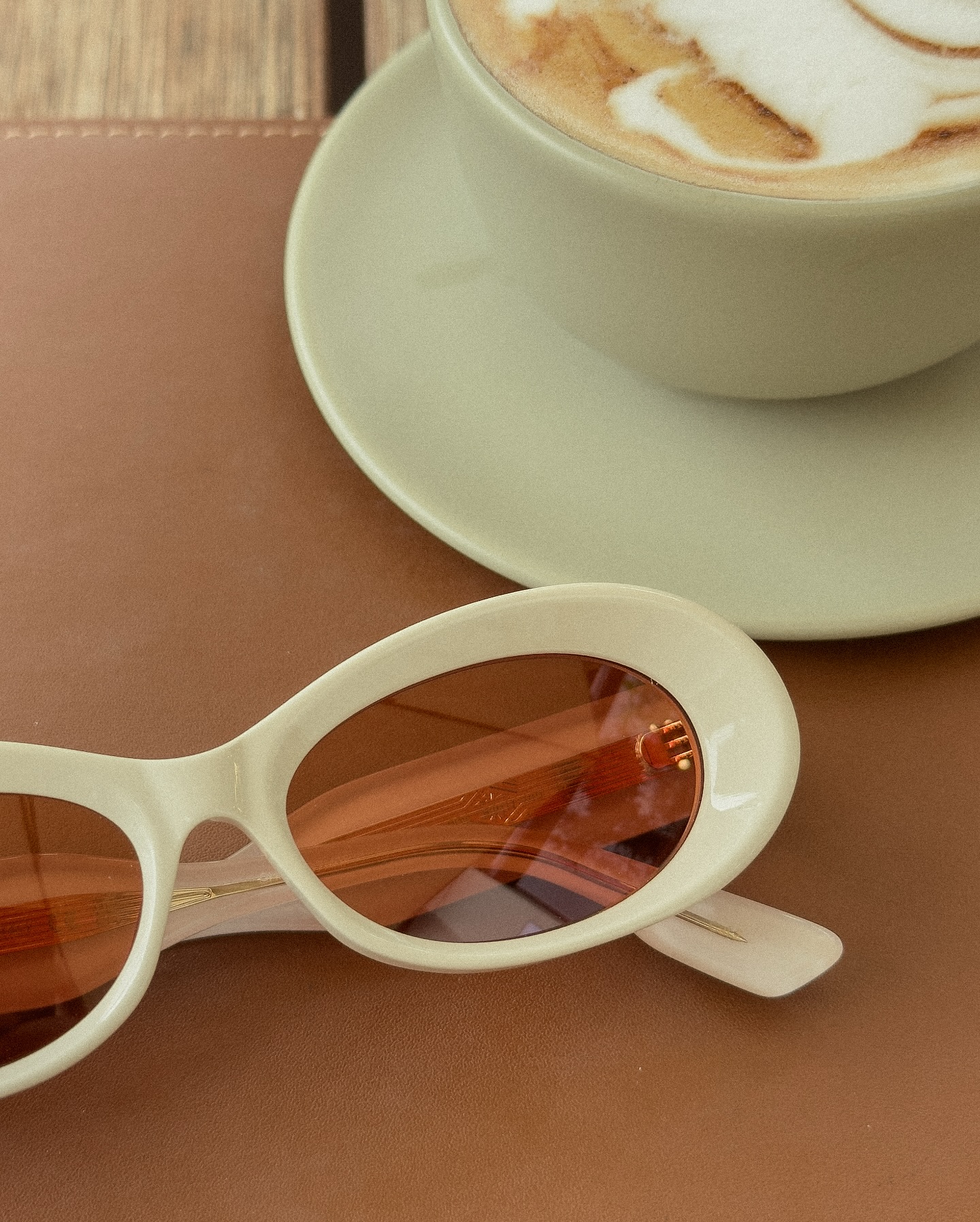 Óculos de sol claros fotografados pela Grendelli ao lado de um café